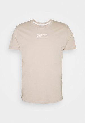 Camiseta de algodón beige con cuello redondo y mangas cortas. Presenta un logo blanco "ALPHA INDUSTRIES" en el pecho. Textura suave.