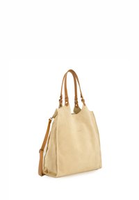 Sac en daim beige avec des poignées en cuir lisse, grand compartiment principal et bandoulière réglable. Présente un détail de marque minimal.