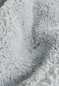 Miękki, jasnoszary polar z teksturowaną, puszystą powierzchnią. Materiał jest gruby i pluszowy, z gęsto uloopowanymi włóknami.