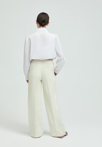 White cropped blouse with slightly puffed sleeves, paired with light textured wide-leg pants. The outfit features a clean, minimalist design.