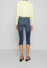 Mörkblå denim capri-byxor med en figursydd design och fållade benslut, kombinerat med en ljusgul långärmad topp med ryggsömn.