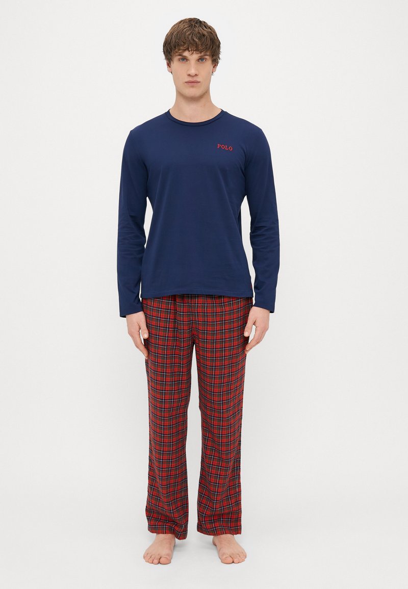 Camisola de manga longa azul-marinho com o logótipo "POLO" vermelho, combinada com calças de pijama em padrão xadrez vermelho e preto. Ambos feitos de um tecido suave e confortável.