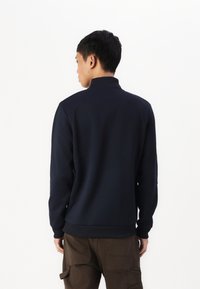 Felpa blu navy con colletto alto, maniche lunghe e polsini a costine, abbinata a pantaloni cargo marroni. Texture liscia, vestibilità classica.