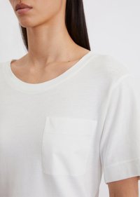White short-sleeve t-shirt made of soft fabric, featuring a simple crew neck and a left chest pocket with a smooth texture.