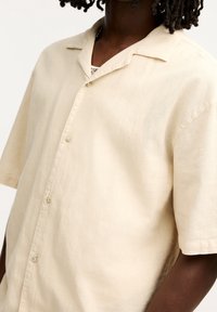 Kortärmad skjorta med knappar i ljusbeige linne. Har en notchad krage och en avslappnad passform. Slät textur med subtil lyster.