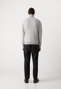 Pull en laine gris avec un col montant, des poignets et un ourlet côtelés, associé à un pantalon noir et des chaussures noires, vu de derrière.