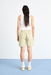 Lys grønne shorts med elastisk liv, teksturert stoff og sidestriper. Modell iført en hvit tank tops og joggesko, sett bakfra.