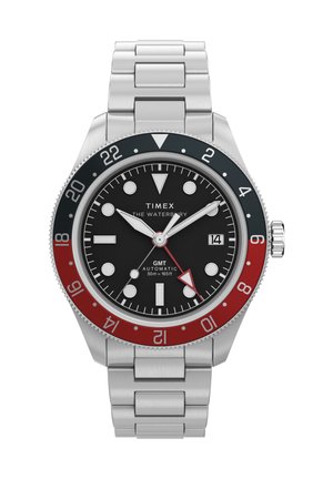 Ατσάλινο ρολόι Timex Waterbury GMT με μαύρο καντράν, κόκκινο και μαύρο στεφάνι 24 ωρών, ασημένιους δείκτες, παράθυρο ημερομηνίας και μπρασελέ από μεταλλικούς κρίκους.