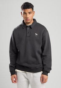 Black sweatshirt with a polo collar, three buttons, and NYC logo. Made of textured fabric, featuring a relaxed fit and ribbed cuffs.