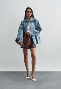 Lichtblauwe spijkerjasje over wit topje, zwarte leren rok en witte hakken. Bruine leren tas met gouden hardware. Lang haar en zonnebril.