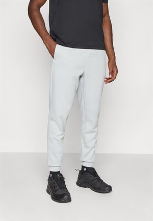 Hellgraue Sweatpants aus weichem Stoff, schmaler Schnitt, elastische Bündchen, kombiniert mit schwarzen Sportschuhen. Einfaches Design ohne sichtbare Muster.