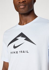 Svetlo modra majica s kratkimi rokavi iz bombaža z okroglim izrezom, ki vsebuje velik črn grafični motiv gore in besedilo "NIKE TRAIL" pod njim.