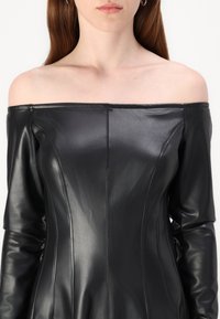 Váll nélküli fekete bőrdzseki, which fitted design with visible seams, smooth texture, and long sleeves.