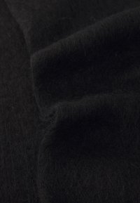 Tissu en laine noir présentant une texture douce et duveteuse avec une apparence légèrement ondulée. La surface montre de fines mèches et une teinte sombre uniforme.