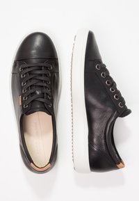 Baskets en cuir noir avec semelles en caoutchouc blanches, bout arrondi et six oeillets ; présentent des accents subtilement marron clair sur le talon et le côté.