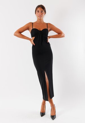 Abito nero aderente con scollatura a cuore, spalline sottili, ritaglio laterale e spacco alto fino alla coscia, realizzato in tessuto liscio ed elasticizzato.