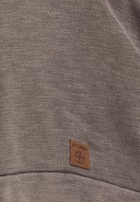 Lichtbruine gebreide trui met een gladde textuur, voorzien van een leren label met de tekst "KEY LARGO" erop gestikt.
