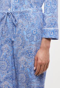 Gaiši zils paisley raksta pidžamu komplekts ar aukliņu jostasvietā. Iekļauj baltu apdari uz roku piedurknēm un pogām. Gluda kokvilnas auduma.