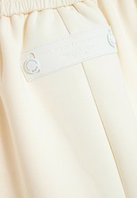 Tela beige con etiqueta rectangular blanca asegurada con dos botones blancos, texto en relieve que dice "Off Design Agency en España."