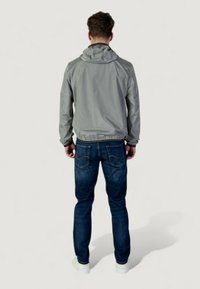 Veste grise légère avec une capuche, des poignets élastiques et une taille élastique, assortie à un jean en denim bleu foncé et des chaussures blanches.