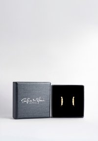 Orecchini in oro con un design curvo e piccole pietre bianche, esposti in una scatola per gioielli nera e testurizzata con interno in velluto.