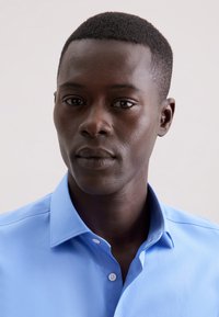 Lichtblauw overhemd met knopen en een kraag, gemaakt van gladde stof. Heeft een gestructureerd ontwerp en zichtbare knoopdetails bij de hals.