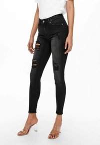 Jeans skinny negros hechos de denim, con desgarros desgastados en los muslos, una cintura alta y un dobladillo deshilachado. Llevados con tacones de tiras transparentes.