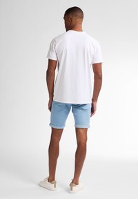 Camiseta blanca de manga corta, pantalones cortos de dobladillo enrollado en azul claro y zapatillas beige con un acento en el talón en contraste. Sin patrones ni gráficos visibles.