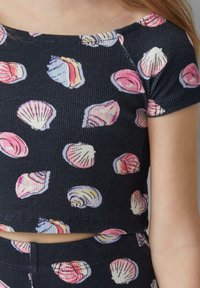 Zwart cropped top met een geribbelde textuur, voorzien van een schelpenpatroon in roze en wit. Het heeft een ruime halslijn en korte mouwen.