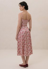 Różowa midi sukienka w kwiaty z marszczonym topem, cienkimi ramiączkami i zwiewnym dołem. W połączeniu z burgundowymi balerinkami. Gładka tekstura tkaniny.
