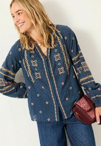 Navyblaue Bluse mit langen Ärmeln, die mit gestickten Blumenmustern in Rot, Grün und Gelb verziert ist. Der Stoff hat eine strukturierte Oberfläche.