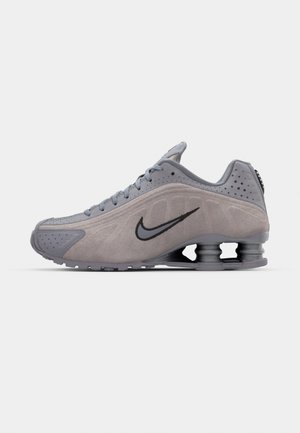 Sive sive tenisice s kuglastim dizajnom, koje imaju čipku za zatvaranje, crni swoosh logo i vidljivu jedinicu za ublažavanje udaraca u peti.
