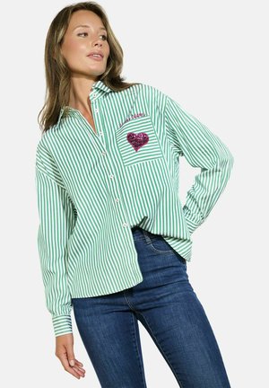 Green and white striped shirt, buttoned, with a chest pocket featuring a pink sequined heart. Long sleeves with cuff details. Fabric appears smooth.