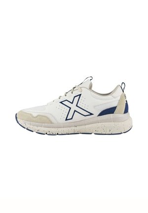 Zapatilla deportiva blanca con acentos en azul marino, parte superior de malla texturizada, puntas de ante y suela de goma salpicada. Presenta un prominente logotipo de "X".