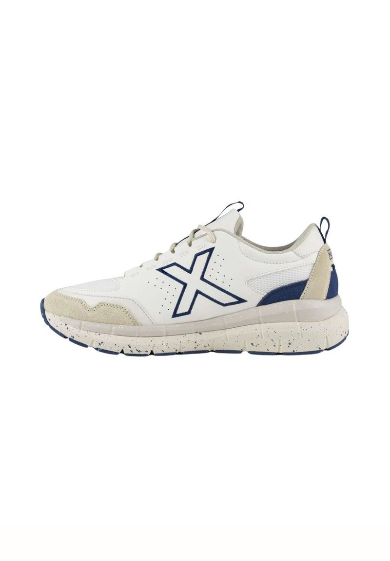 Zapatilla deportiva blanca con acentos en azul marino, parte superior de malla texturizada, puntas de ante y suela de goma salpicada. Presenta un prominente logotipo de "X".