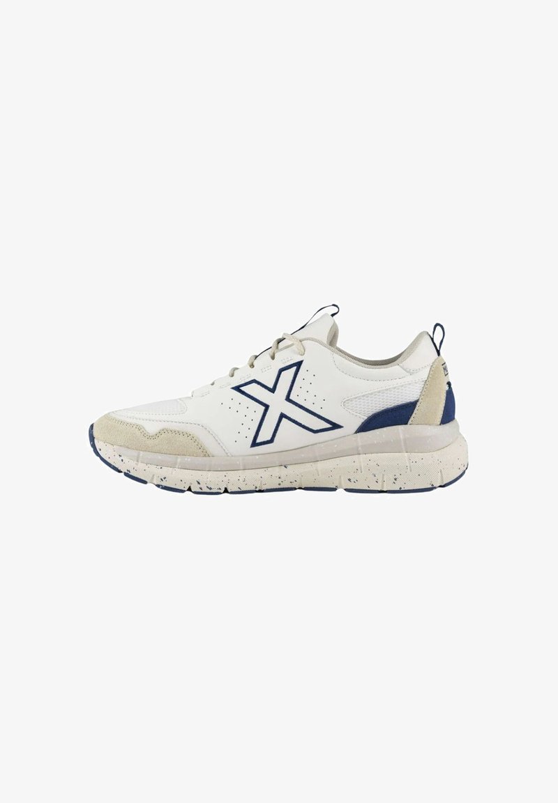 Zapatilla deportiva blanca con acentos en azul marino, parte superior de malla texturizada, puntas de ante y suela de goma salpicada. Presenta un prominente logotipo de "X".