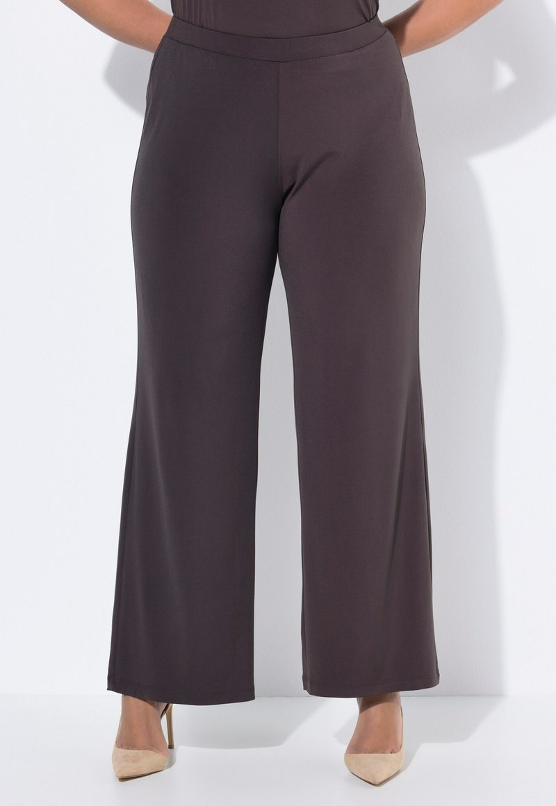 Wijde broeken in donkerbruin stof met een gladde textuur en een elastische tailleband, gecombineerd met neutrale hoge hakken.