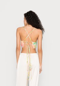 Top bikini senza schienale multicolore con spalline incrociate regolabili e dettaglio a fiocco. Il materiale appare liscio con un motivo floreale.