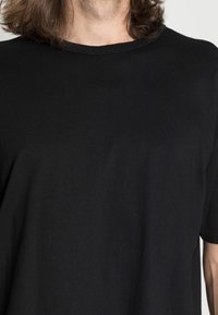 Camiseta negra de manga corta, elaborada en algodón suave, con escote redondo y detalles de costura mínimos en las mangas y el dobladillo.