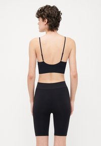 Black seamless sports bra with thin adjustable straps, paired with high-waisted black shorts that have a smooth texture and  thigh-length fit.
