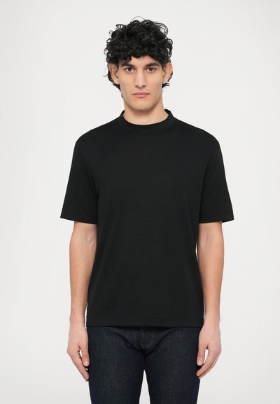 Zwart T-shirt met korte mouwen en een ronde hals, voorzien van een subtiele textuur, gecombineerd met donkerblauwe spijkerbroek. Eenvoudig ontwerp zonder zichtbare logo's.