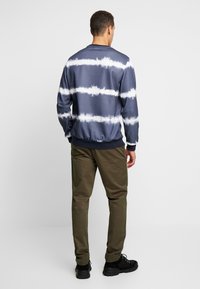 Niebieska bluza tie-dye z białymi paskami, okrągły dekolt, ściągacze na mankietach i u dołu. Noszona z oliwkowozielonymi spodniami i czarnymi tenisówkami.