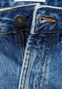 Modre kavbojke v fokusu, z zadrgo, kovinsko gumbom z blagovno znamko in kontrastnim oranžnim šivom ob šivih.