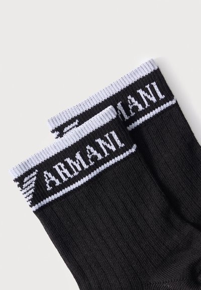 Μαύρες ριγωτές κάλτσες με λευκή περίγραμμα στην κορυφή, με το κείμενο "ARMANI" και το λογότυπο αετού της Armani σε λευκό.