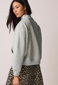 Grå sweatshirt med høj krave, faldende skuldre og ribbede manchetter, parret med en leopardmønstret nederdel. Blødt, struktureret stof.