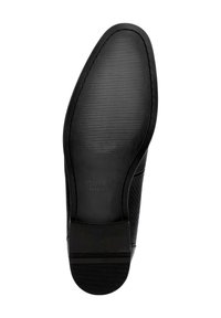 Suela de zapato de cuero negro con acabado texturizado. Presenta bordes suaves y un logo central. Líneas de agarre de goma para tracción.