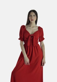 Rød kjole med korte pufærmer og taljebånd, med en smocked bodice og en flydende nederdel, lavet af tekstureret stof.