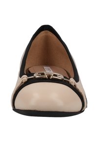Chaussure plate beige avec bordure noire, boucle décorative dorée à l'avant, et doublure intérieure matelassée couleur fauve.