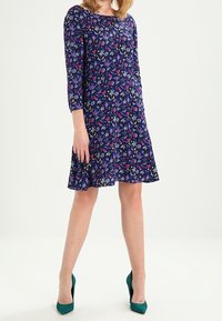 Navy dress with a floral pattern in red, yellow, and green. Features three-quarter sleeves and a flared skirt. Worn with teal heels.