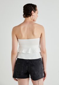 Witte strapless top met een gerimpelde zoom, gecombineerd met zwarte denim shorts met verscheurde randen en twee achterzakken. Glad textuur.